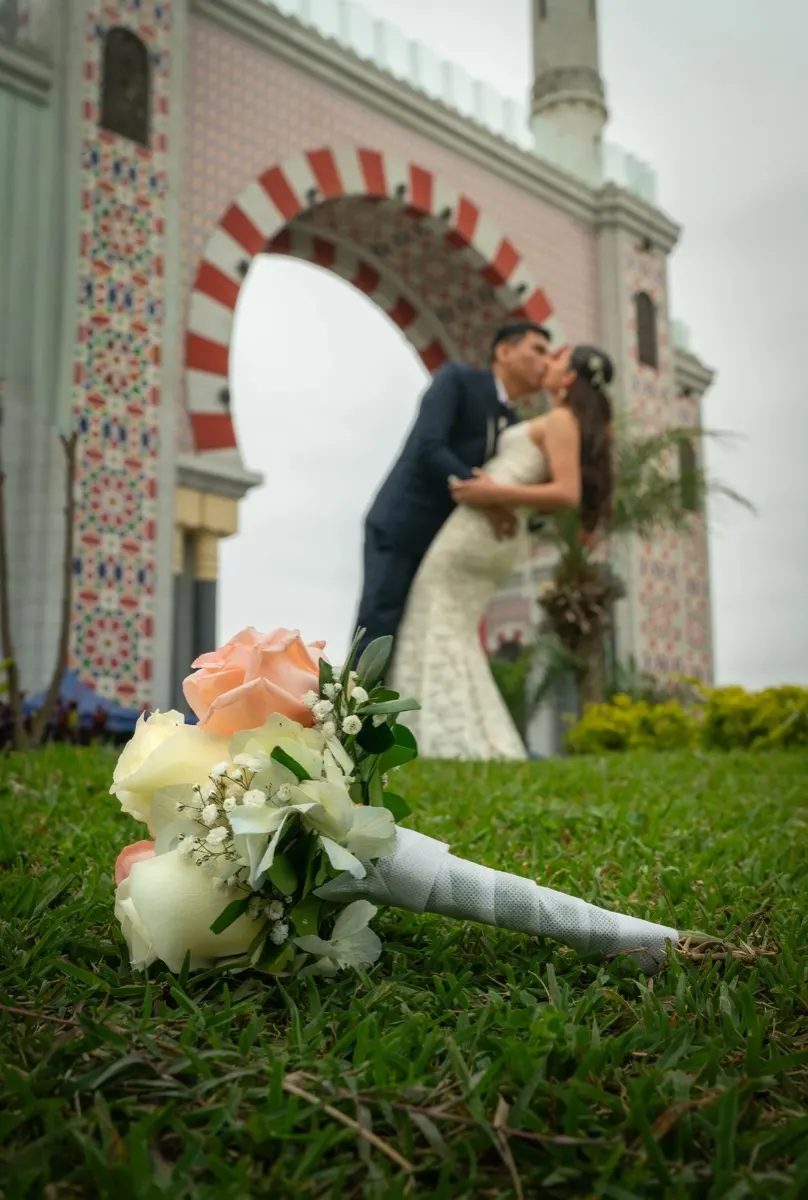 Ramo de novia en el pasto y los novios besándose al fondo